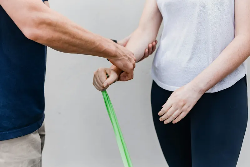 Practitioner guiding a client's arm against light resistance-band tension during a gentle muscle activation exercise
